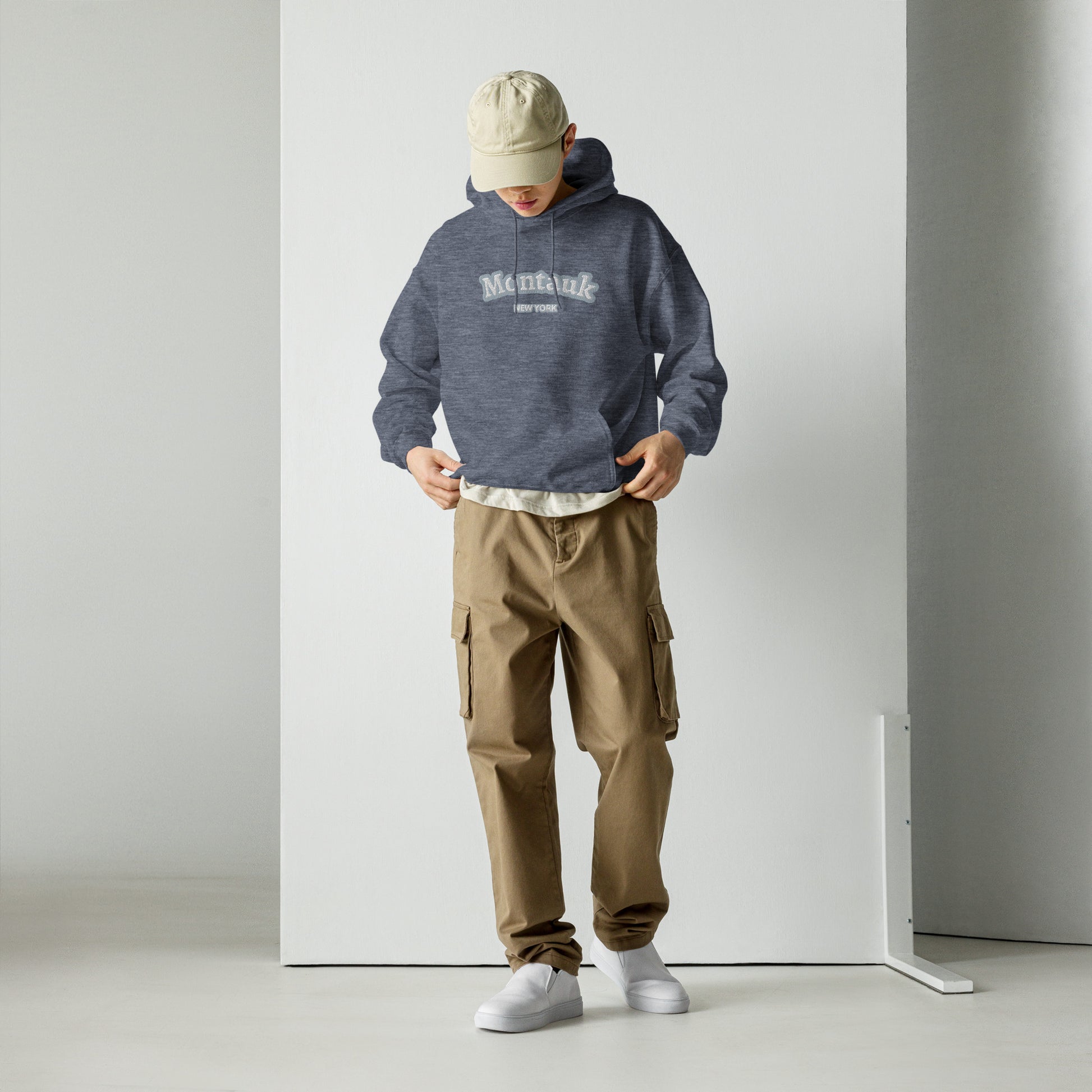 Model wearing Montauk Embroidered Hoodie - Unisex Coastal Sweatshirt in heather navy, styled with khaki cargo pants and white sneakers.